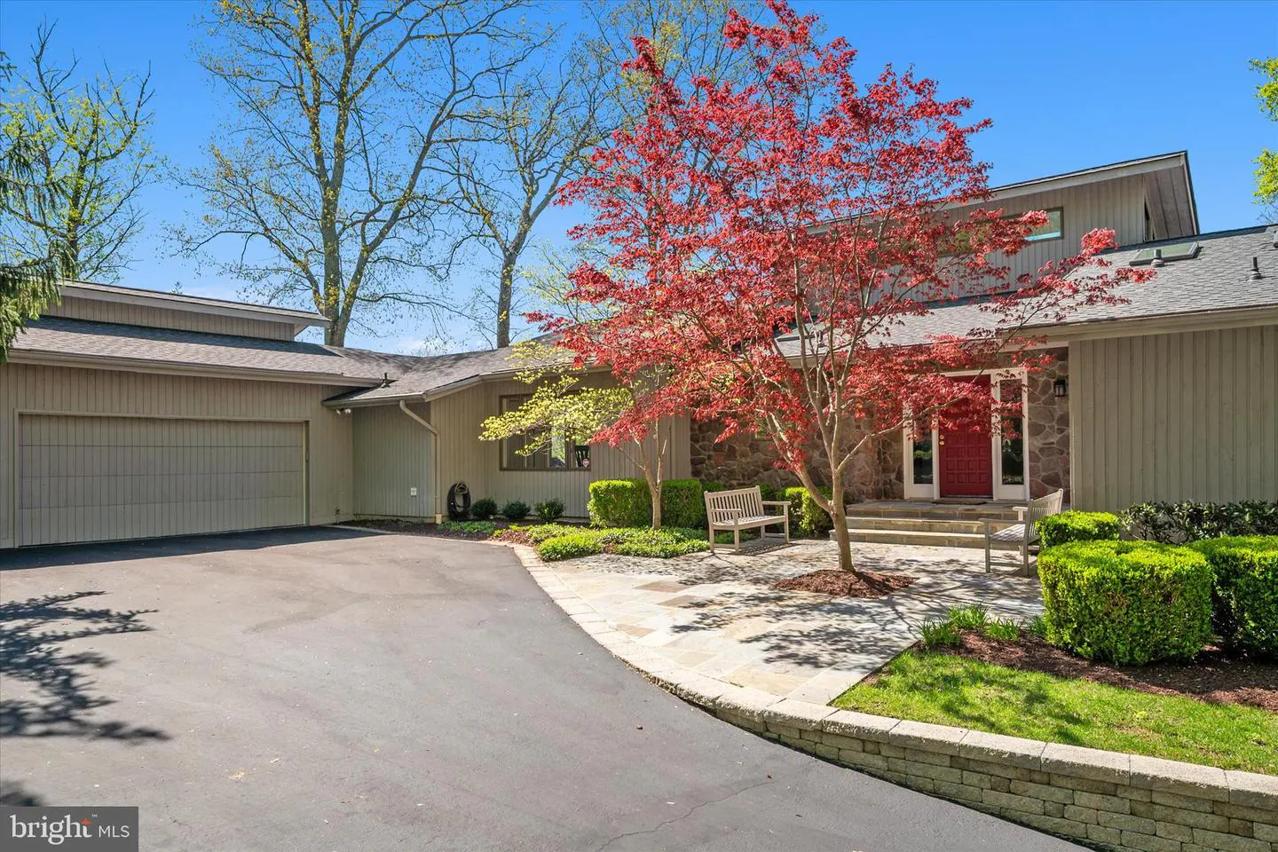 Exterior view of a beige house with a red front door, a red Japanese maple tree, and a black asphalt driveway.
