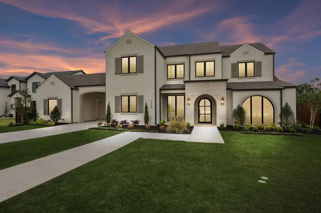 Two-story white house with black trim, gray shutters, and a gray roof at dusk. A green lawn and a concrete walkway lead to the front door.