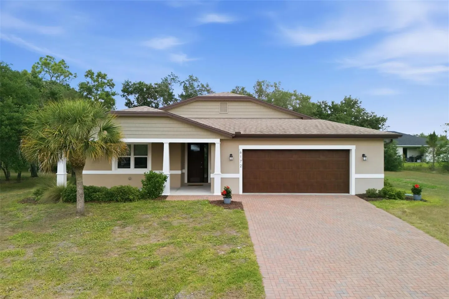 Beige single-story house with a brown garage door and a brick driveway under a blue sky.