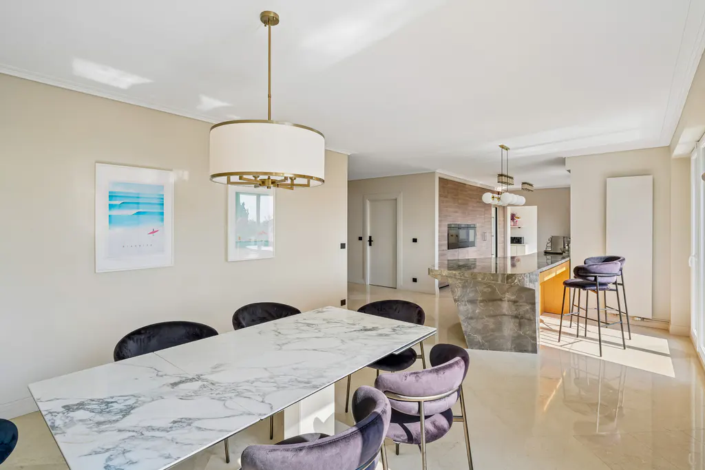 A bright, open-concept dining area with a marble table, velvet chairs, and a view into the kitchen.
