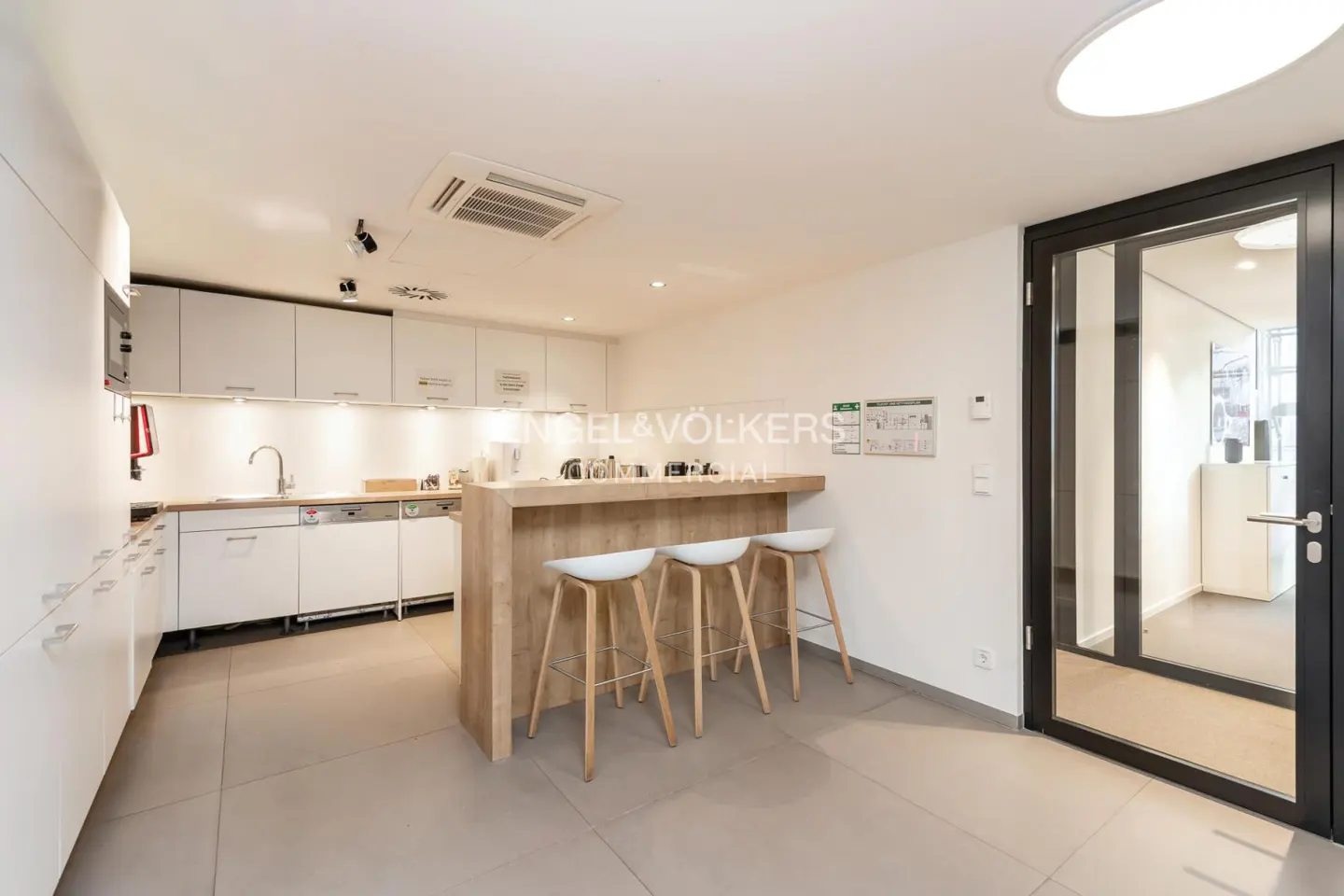 Bright kitchen with white cabinets, wood counter, and three white stools. A black-framed glass door is on the right.