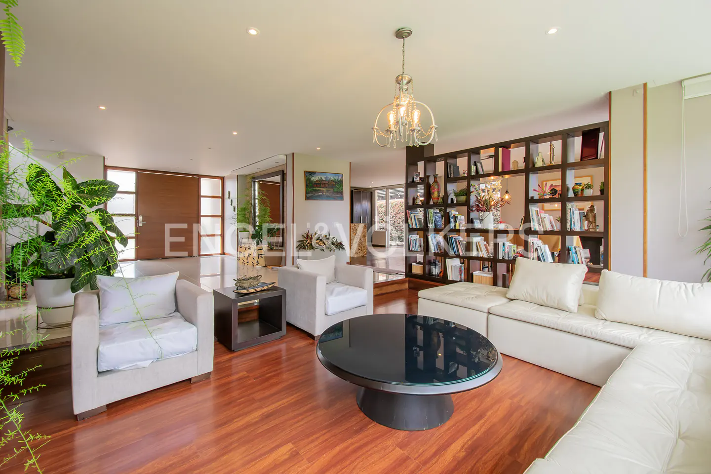 Modern living room with white sofas, a round black coffee table, hardwood floors, and a large wooden bookshelf.