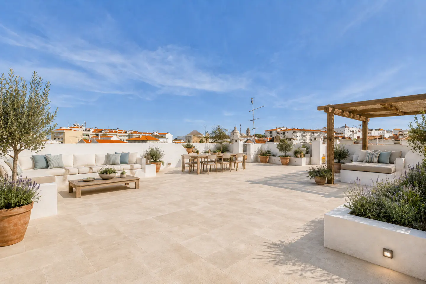 A rooftop terrace with white walls, beige tile, and outdoor furniture under a blue sky.