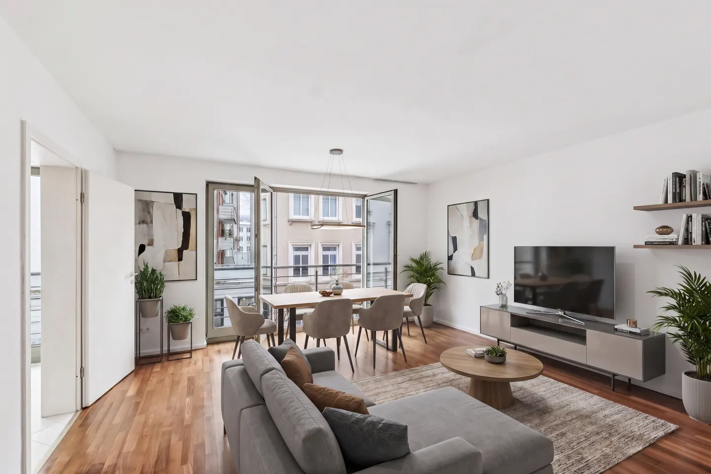 Bright living room with hardwood floors, gray sofa, dining table, TV, and open balcony doors.