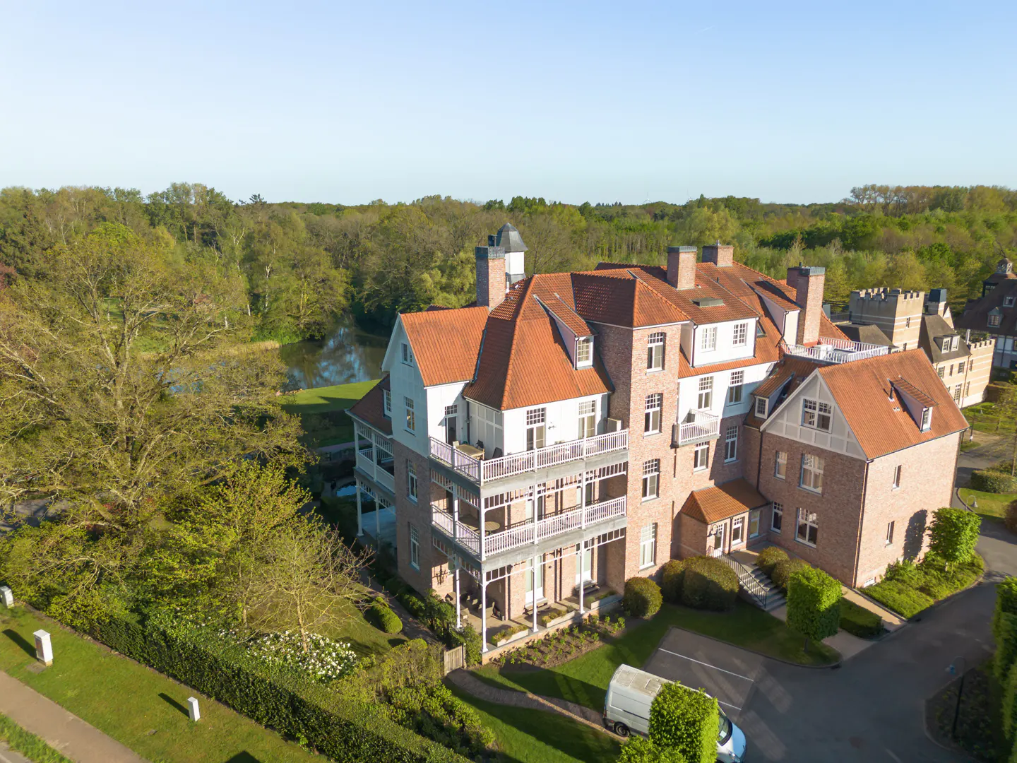 Aerial view of a large brick building with a red tile roof, balconies, and green trees in the background.