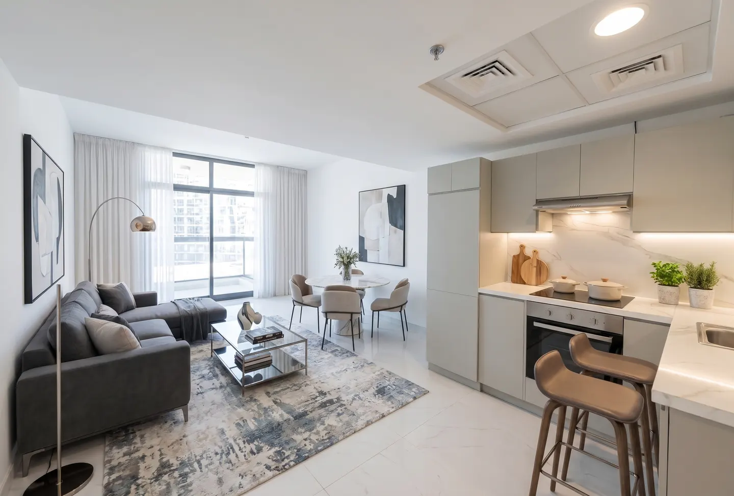 Bright, modern apartment interior with a gray sectional sofa, dining table, and kitchen with bar stools.