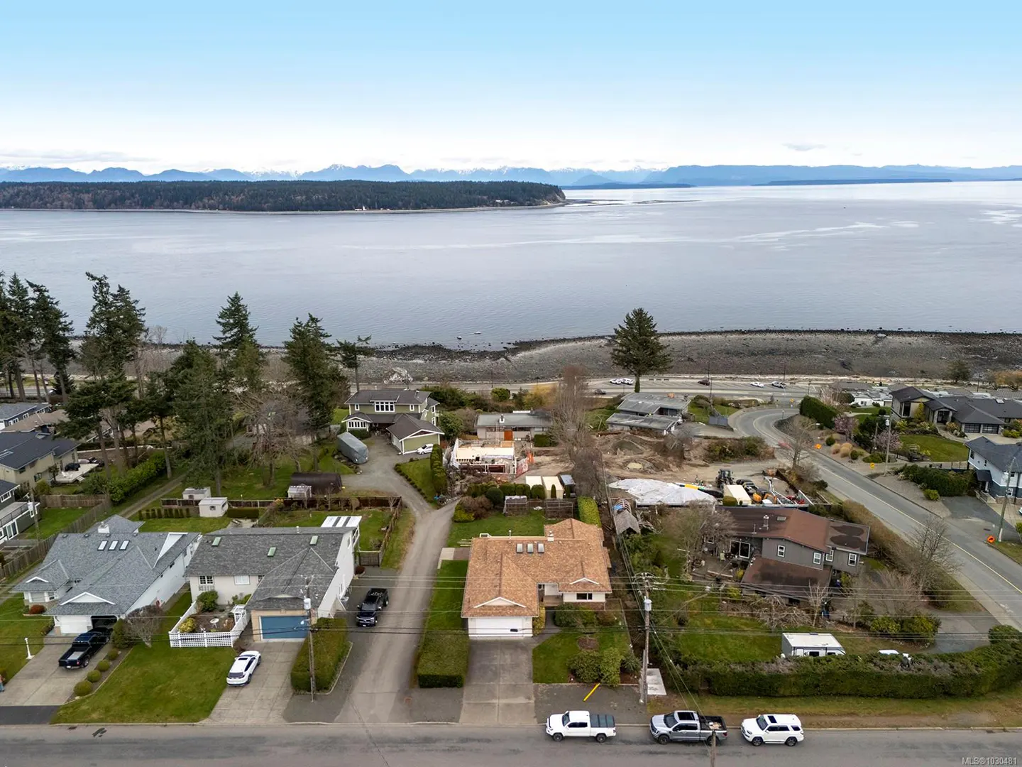 Aerial view of a residential street with houses, cars, and a view of the ocean and mountains in the background.