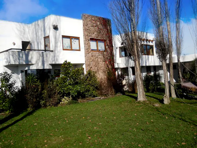 Two-story white house with a stone accent wall, brown window frames, green lawn, and bare trees under a blue sky.