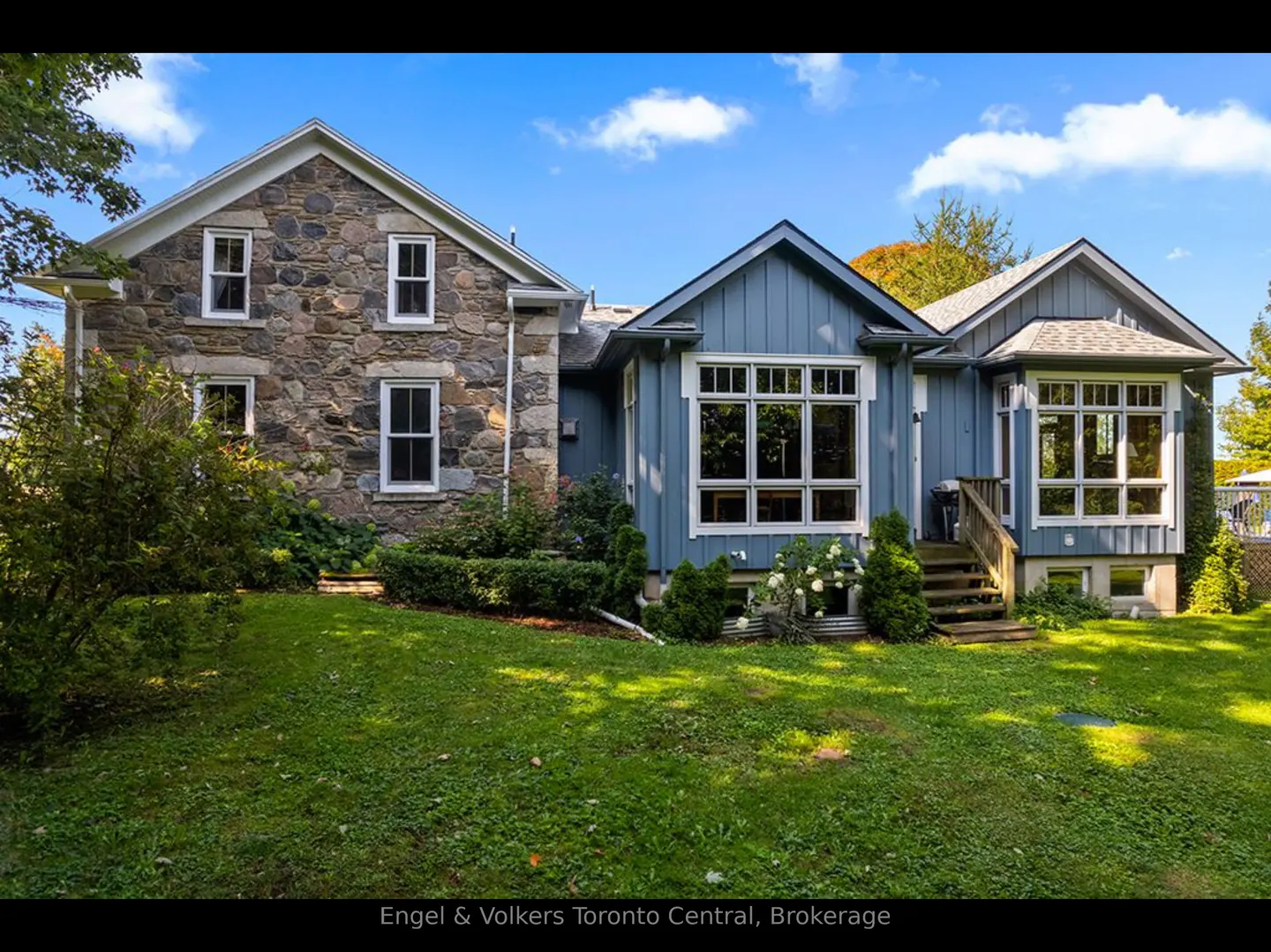 Exterior view of a two-story house with stone and blue siding, white trim, and a green lawn under a blue sky.