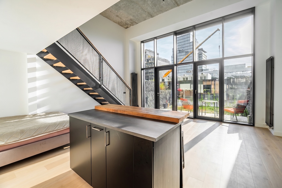 Modern loft with a black kitchen island, floating staircase, and floor-to-ceiling windows overlooking a city patio. [AI-generated text]