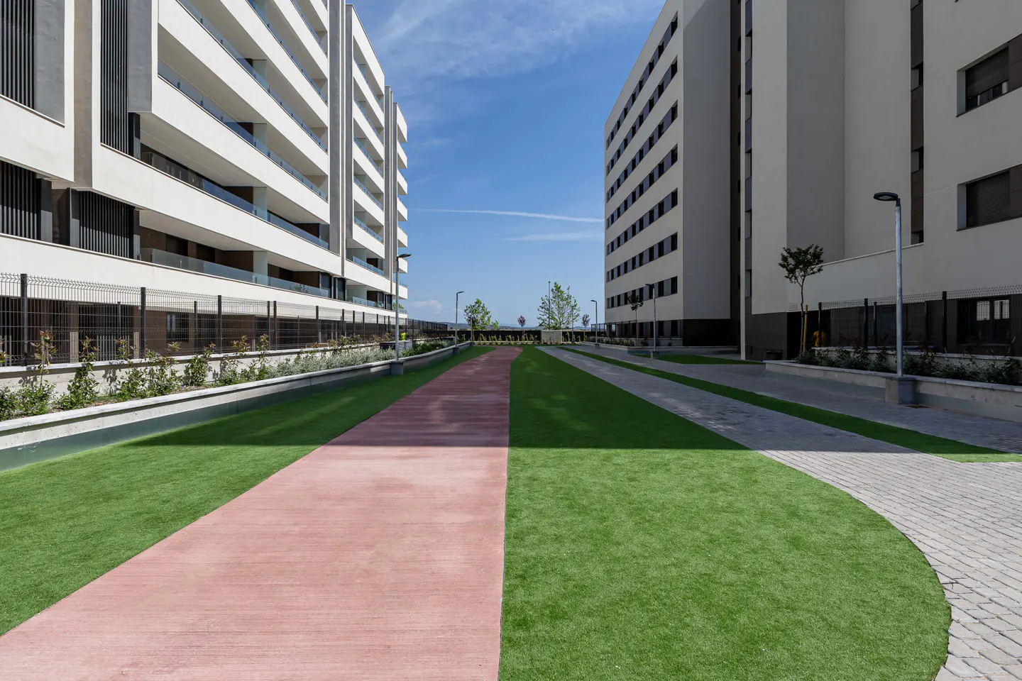 Exterior view of modern white apartment buildings with a red walkway and green grass under a blue sky.