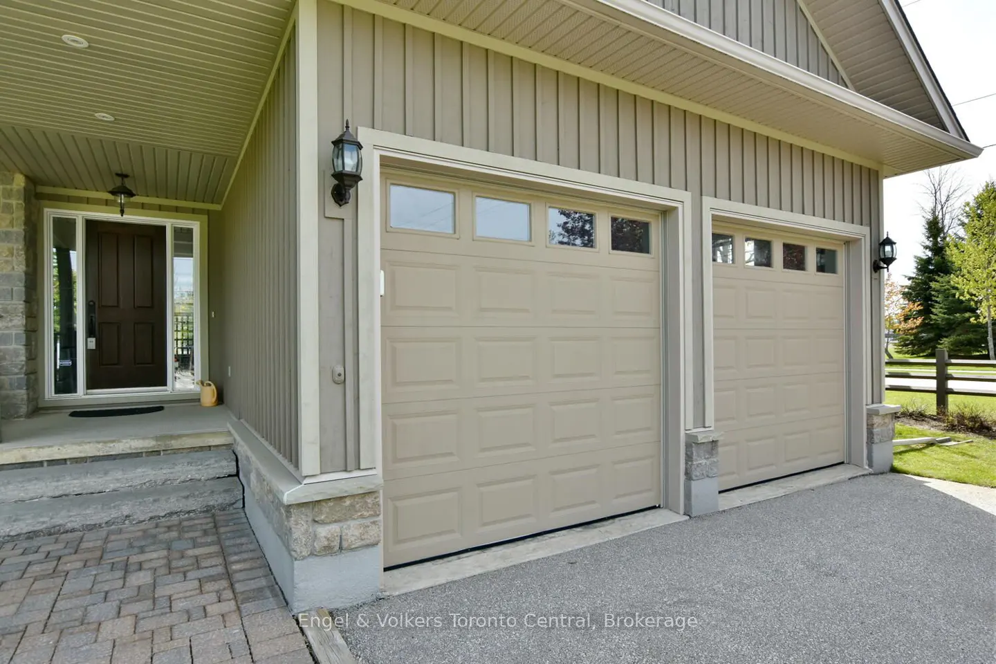 Exterior view of a beige house with a two-car garage, stone accents, and a dark brown front door under a covered porch.