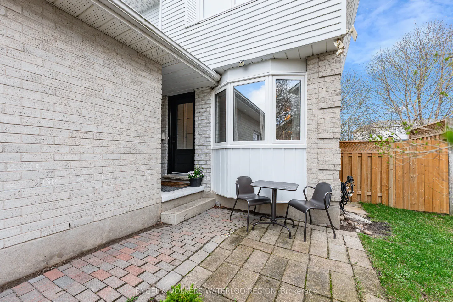 Exterior view of a two-story house with a brick facade, a black front door, and a small patio with a table and chairs.