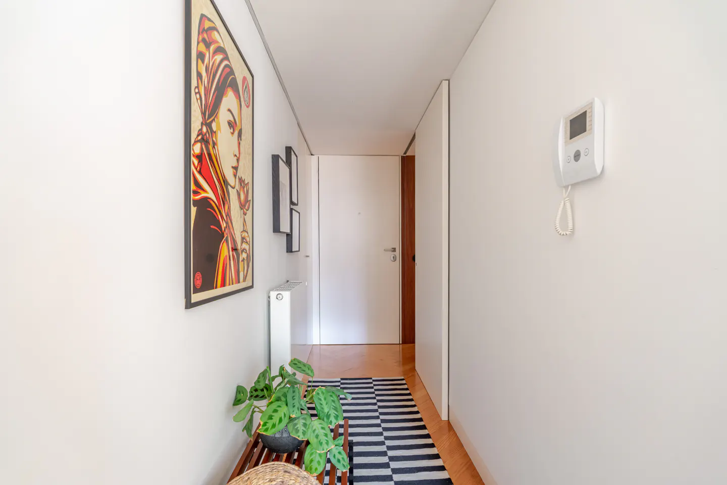 Hallway with white walls, a black and white striped rug, and a framed portrait of a woman in red and yellow.