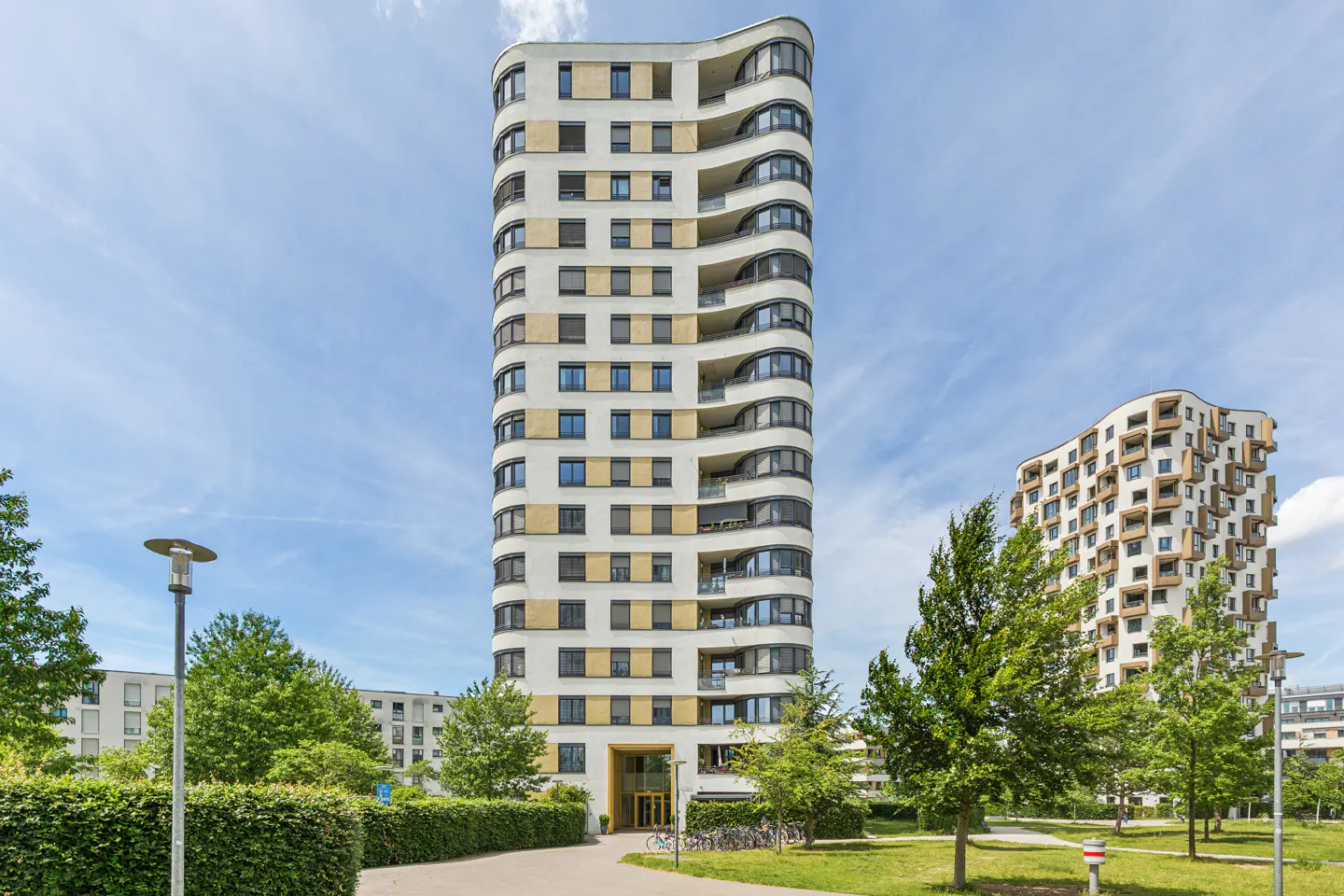 Tall, modern apartment building with curved balconies and beige and white facade under a clear blue sky.