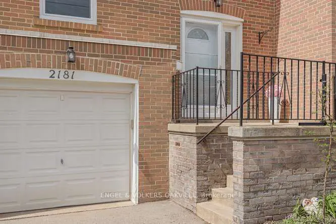 Exterior of a brick house with a white garage door, address 2181, and a front door with black railings.