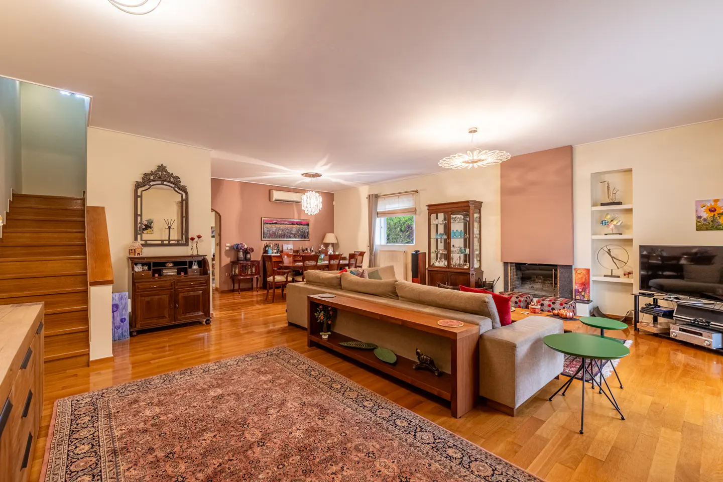A living room with hardwood floors, a large rug, a sofa, and a fireplace. A dining table and chairs are visible in the background.
