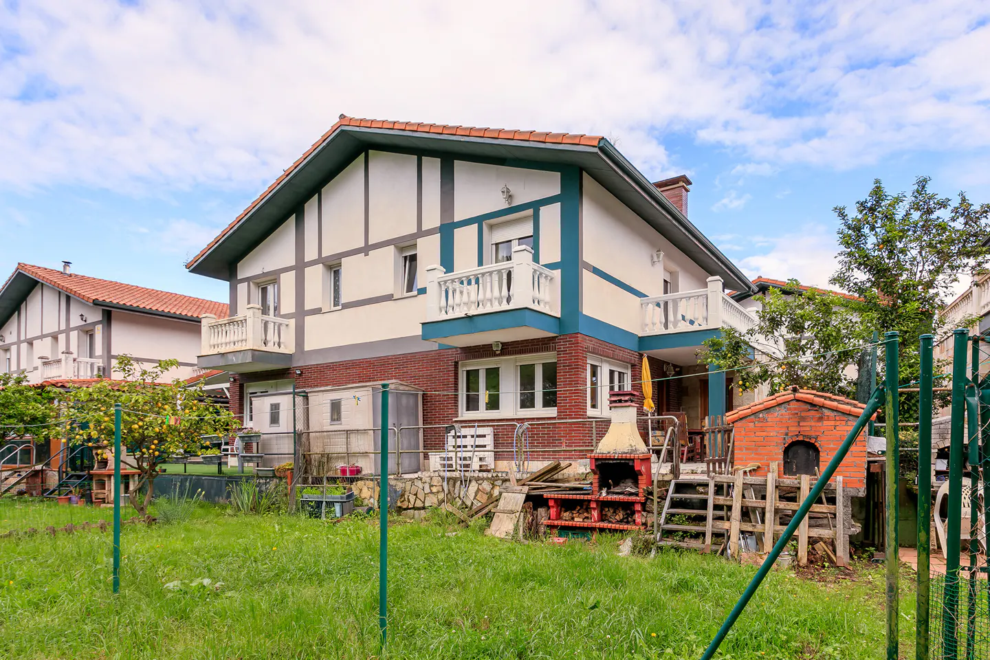 Two-story house with a brick base, white upper level with blue trim, and a red tile roof, seen from the backyard.
