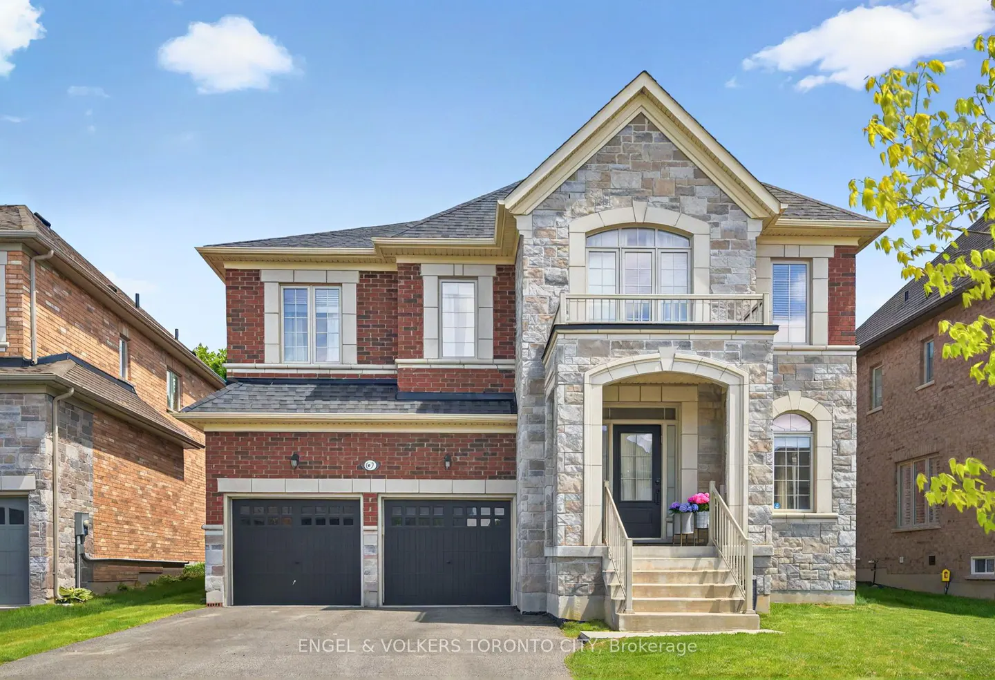 Two-story house with brick and stone exterior, black garage doors, and a small front porch with stairs.