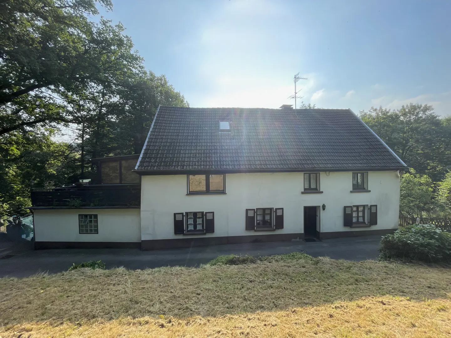 Exterior view of a two-story white house with dark shutters and a gray roof, surrounded by trees and a grassy lawn.