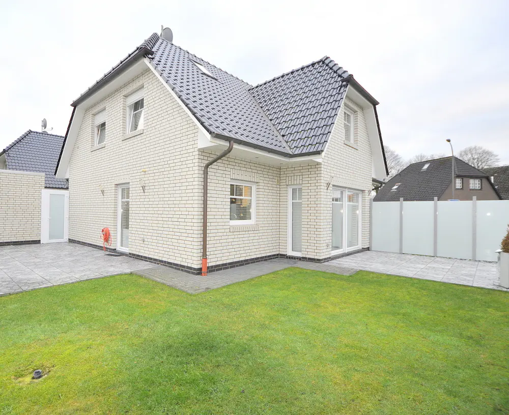 Two-story white brick house with a dark gray roof, green lawn, and gray patio.