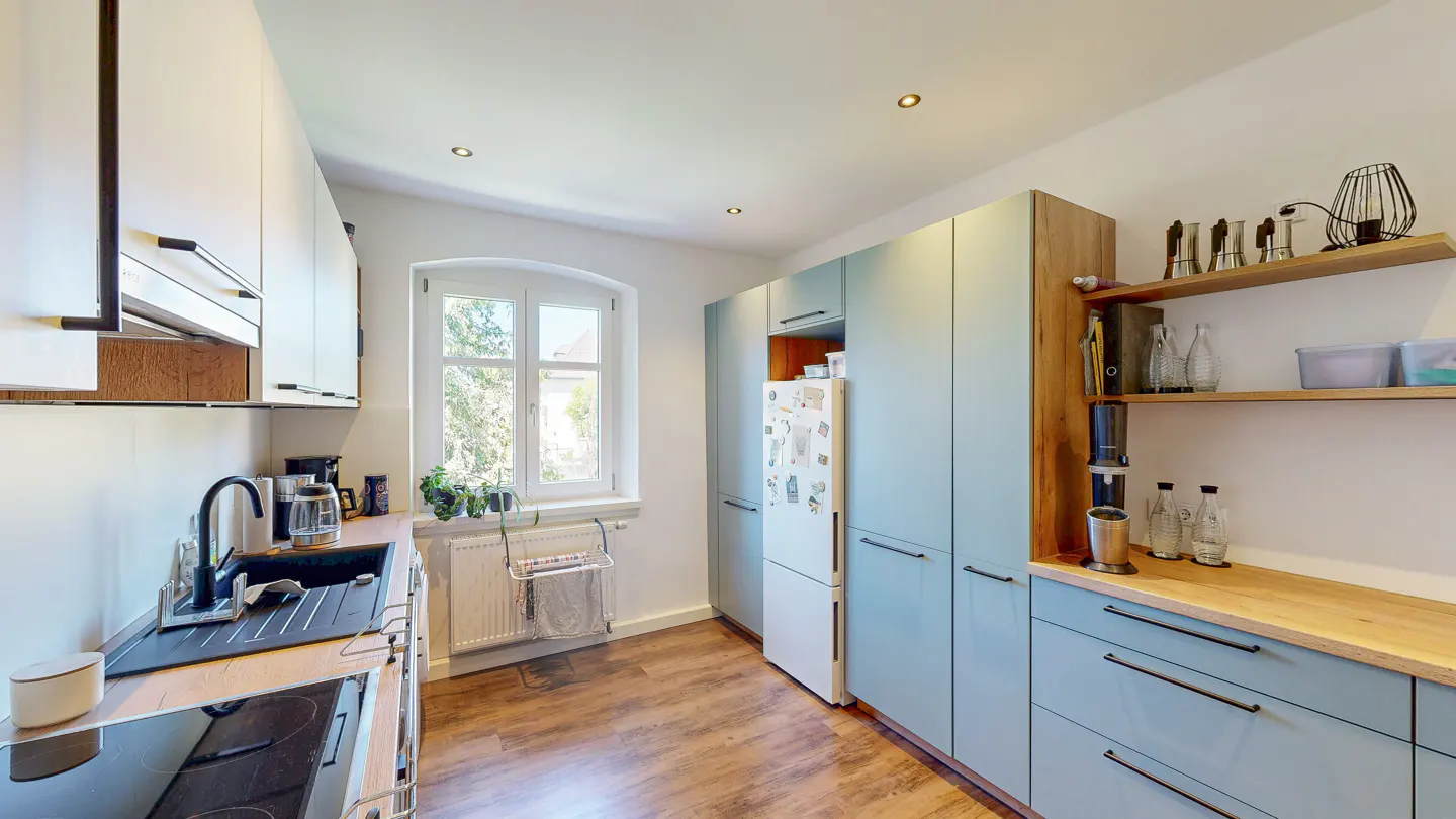 Modern kitchen with light blue cabinets, wood countertops, a white refrigerator, and a window over a radiator.