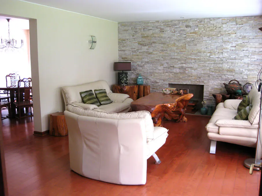 Living room with hardwood floors, stone accent wall, and white sofas. A dining room is visible through an archway.