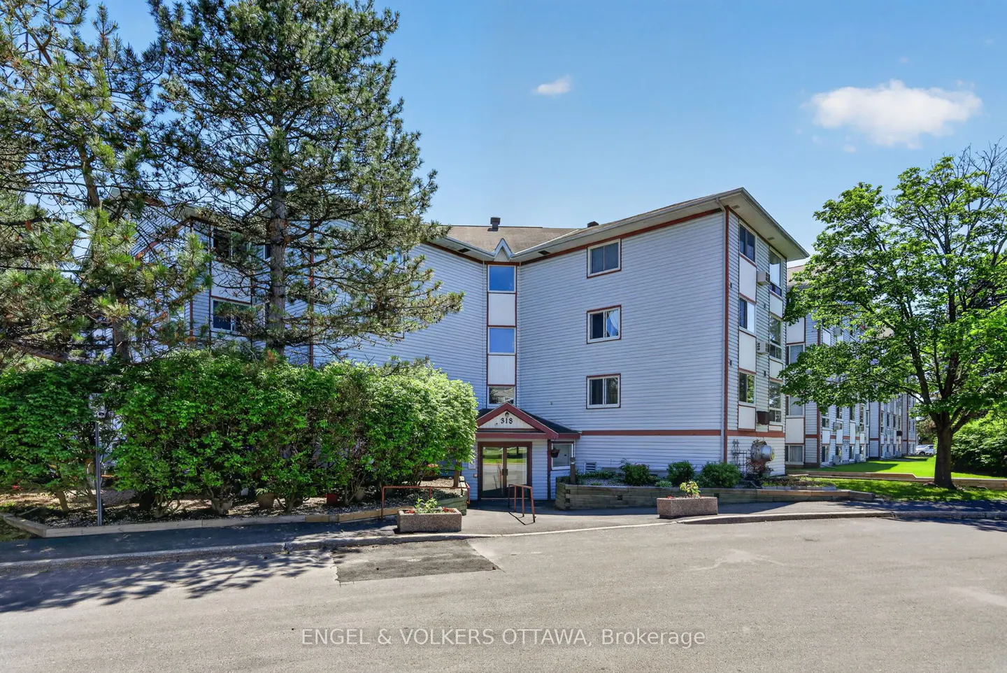 Exterior view of a light blue multi-story apartment building with a paved parking lot and surrounding trees.