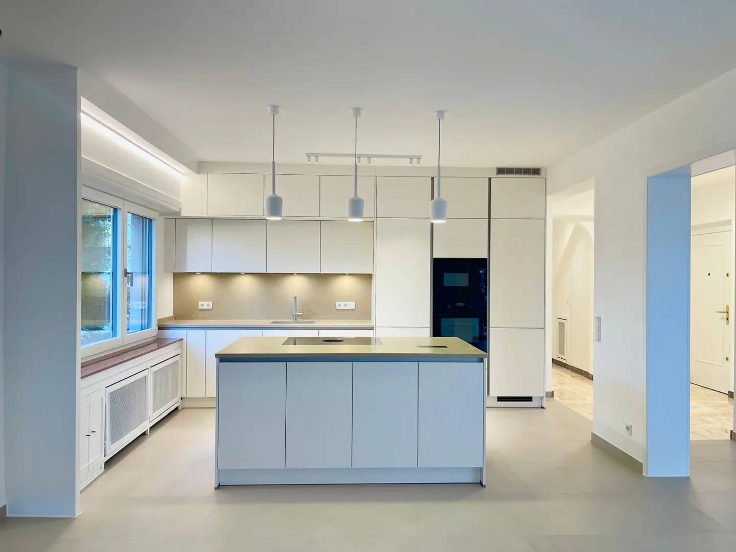 Bright, modern kitchen with white cabinets, island, and pendant lights. A large window provides natural light.