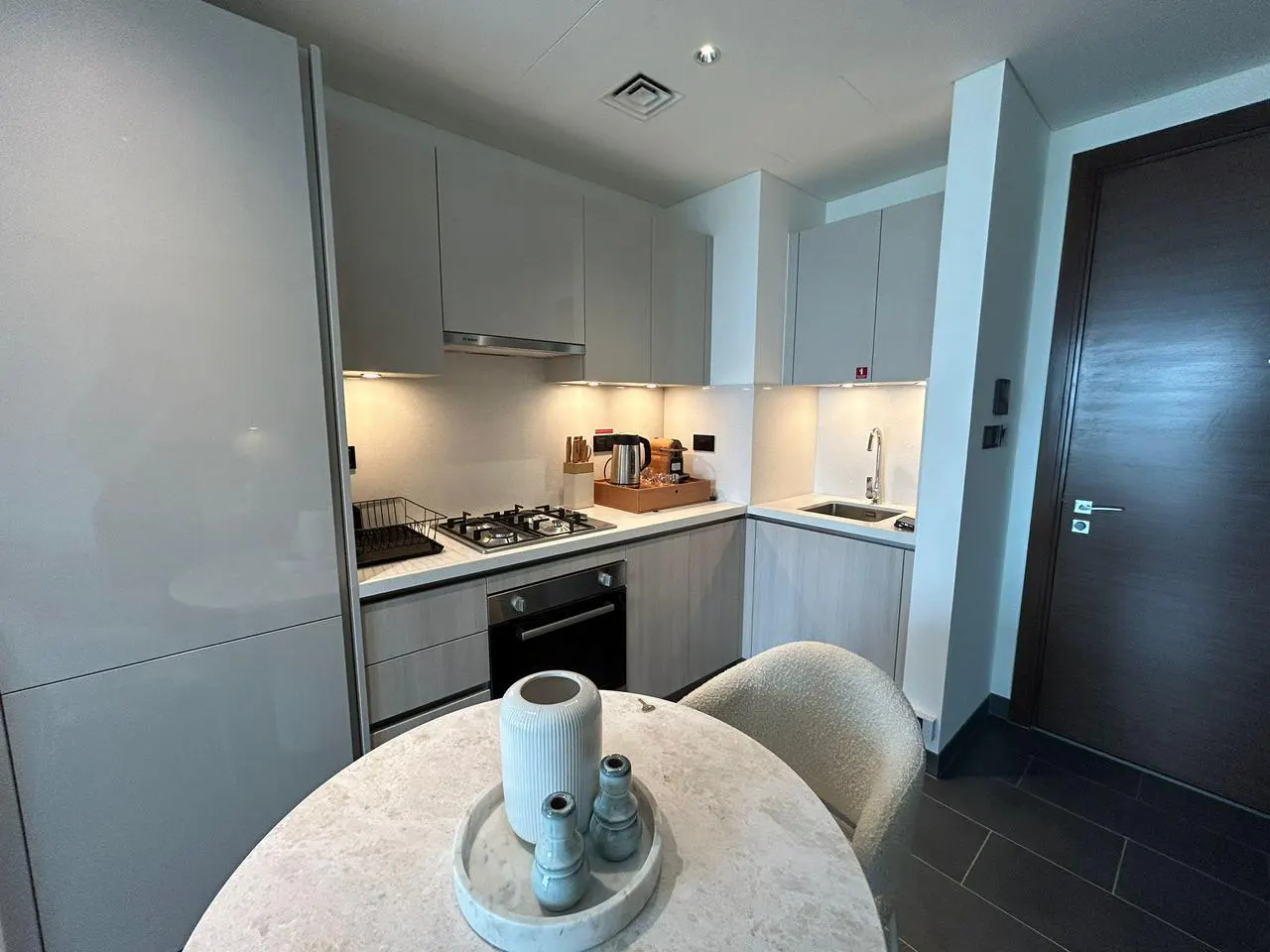 A modern kitchen with gray cabinets, stainless steel appliances, and a round table with decorative vases.