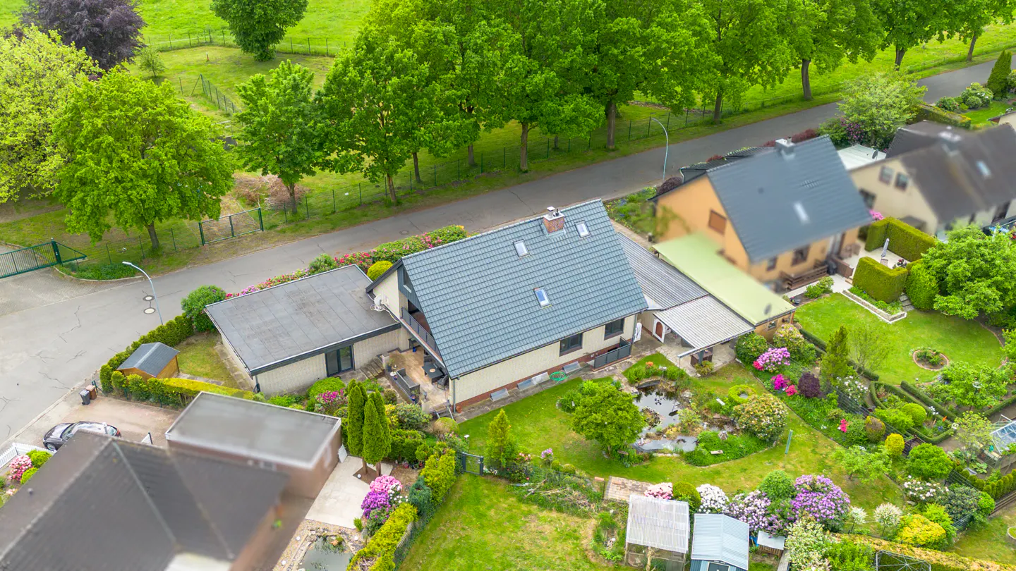 Aerial view of a house with a gray roof and a lush green garden with a pond and colorful flowers.
