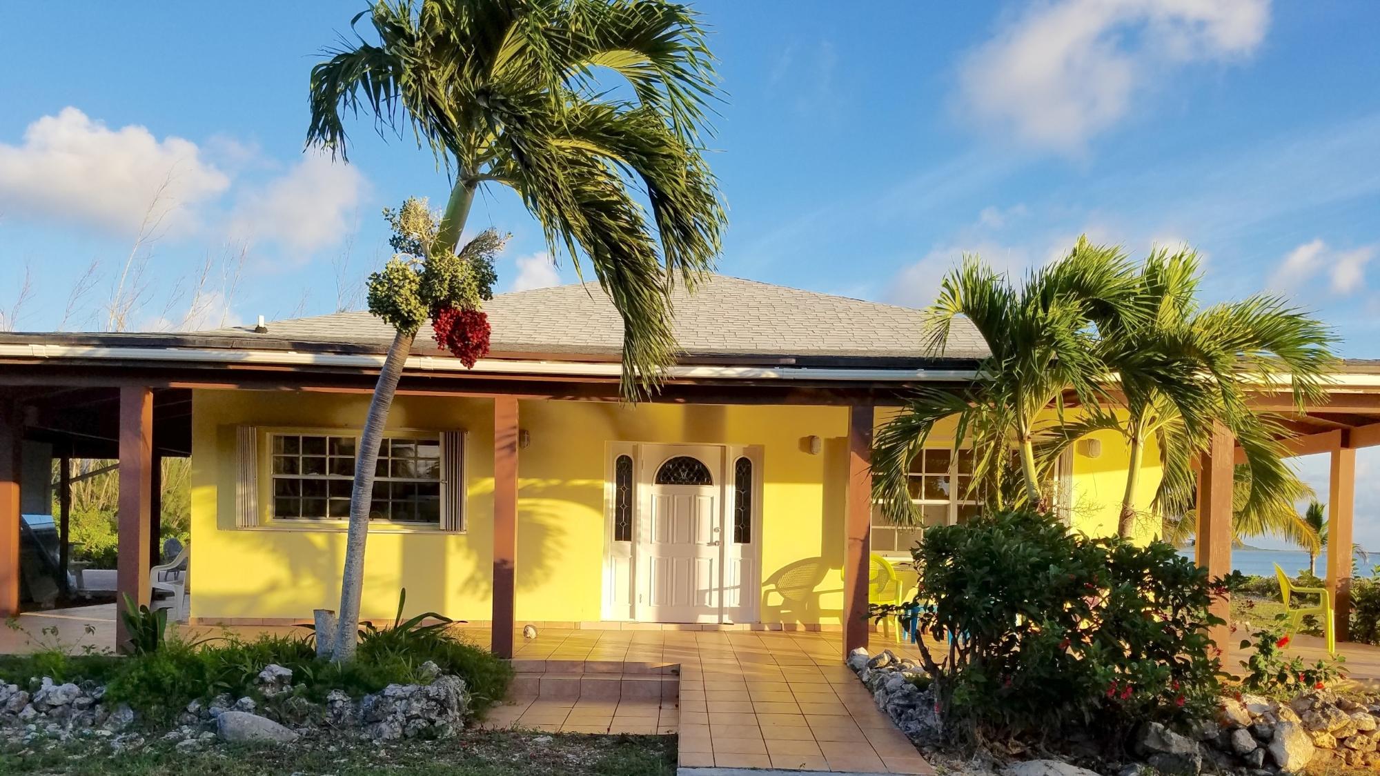 A yellow house with a white door and trim, framed by palm trees under a blue sky.