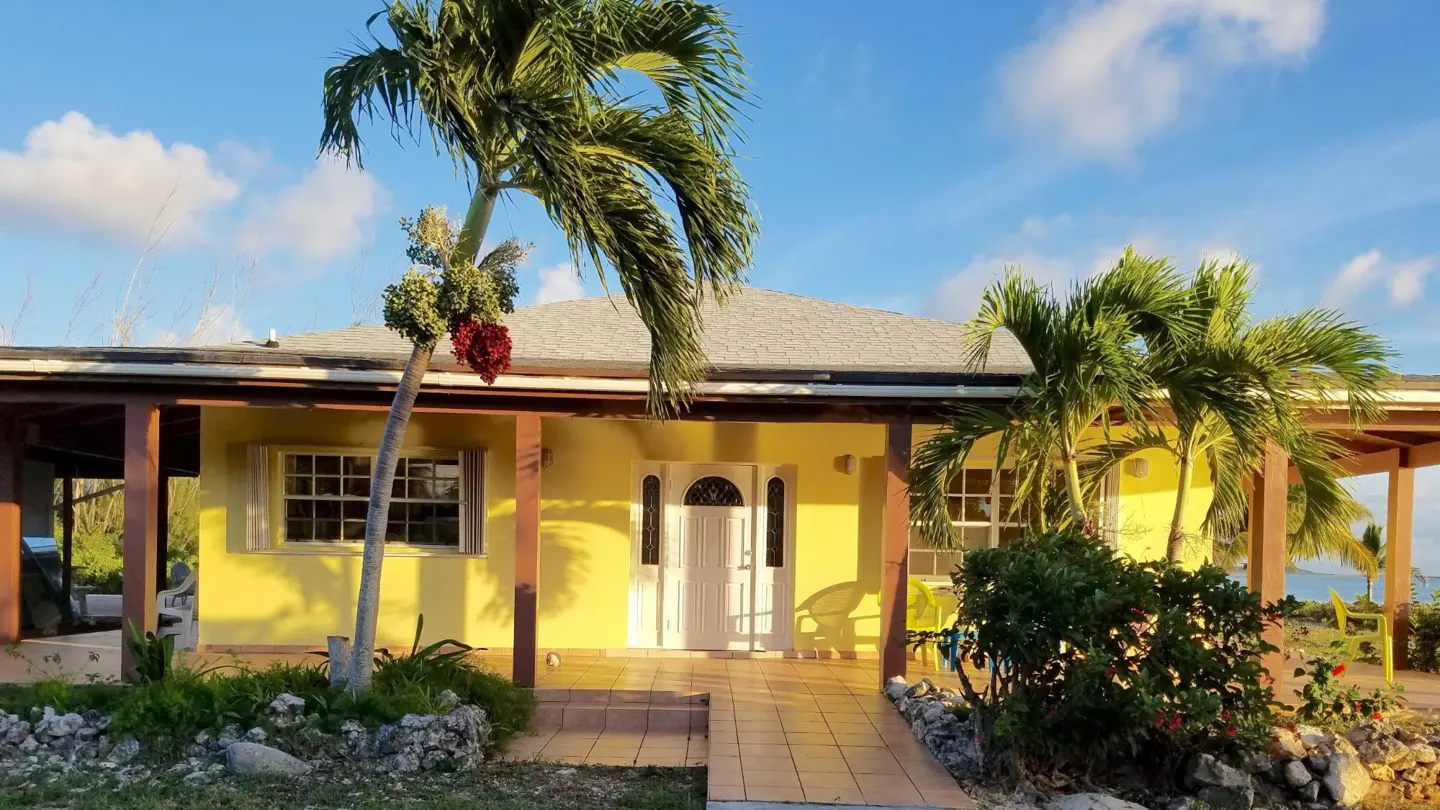 A yellow house with a white door and trim, framed by palm trees under a blue sky.