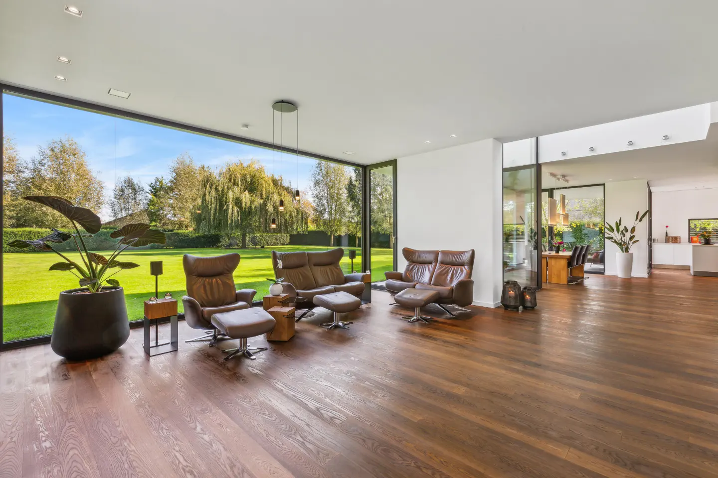 Bright living room with brown leather chairs, hardwood floors, and a large window overlooking a green lawn.