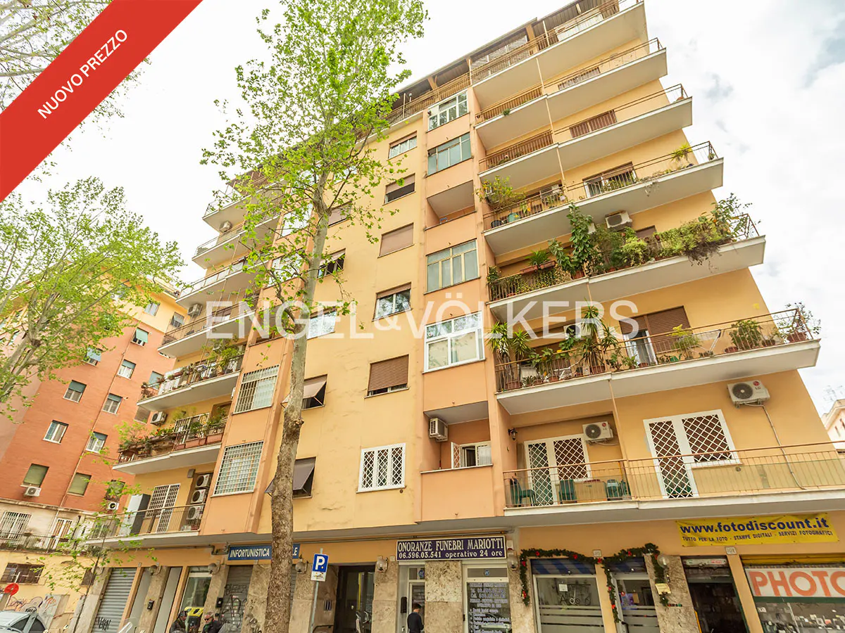 Exterior view of a peach-colored apartment building with balconies and green plants. A red banner reads "NUOVO PREZZO".