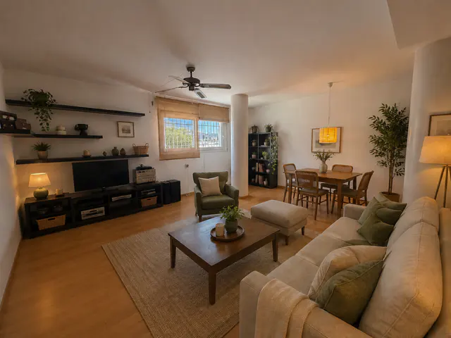 Bright living room with a beige sofa, green armchair, wooden coffee table, dining area, and wall-mounted shelving.