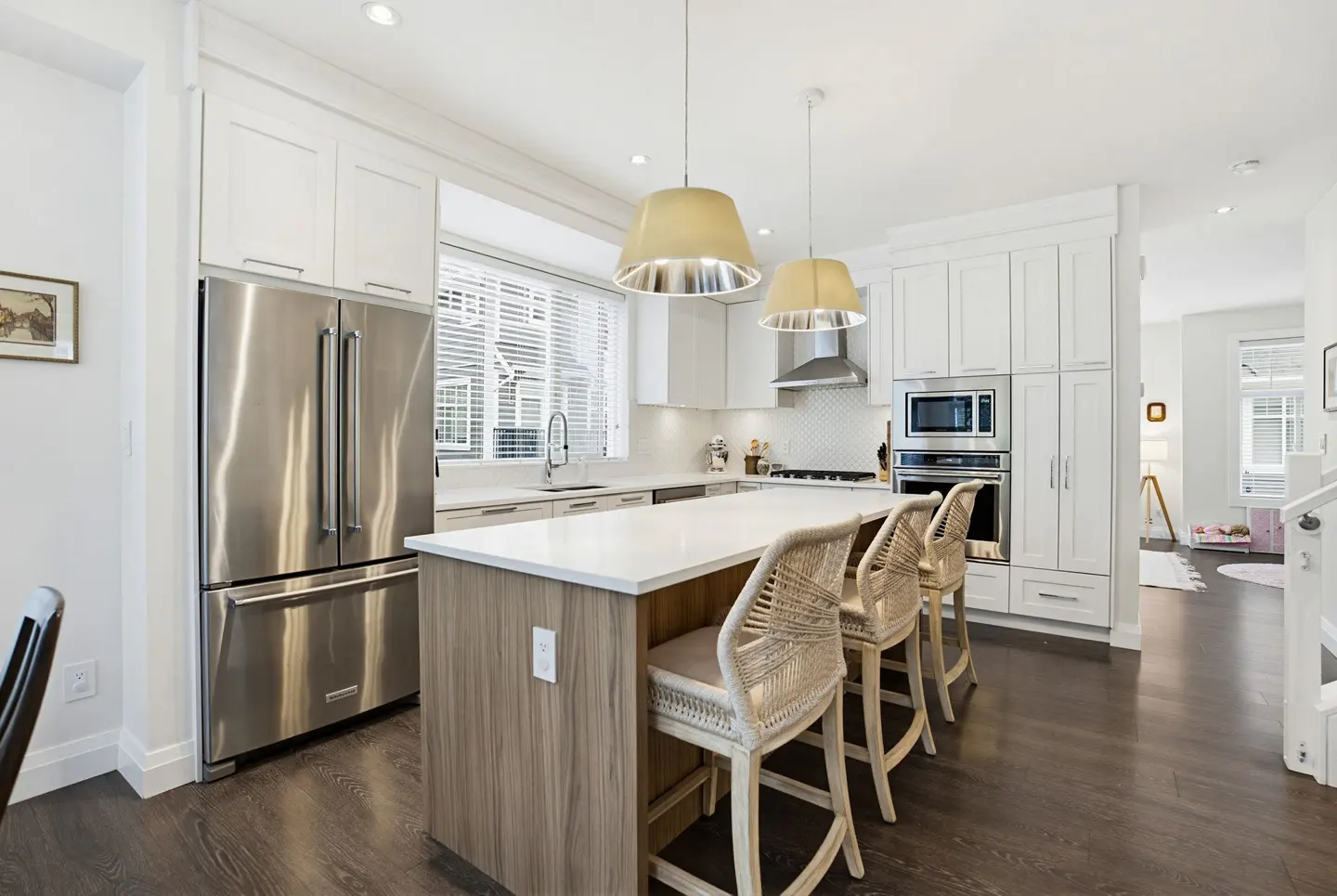 Bright kitchen with white cabinets, stainless steel appliances, and a wood-paneled island with three woven bar stools.