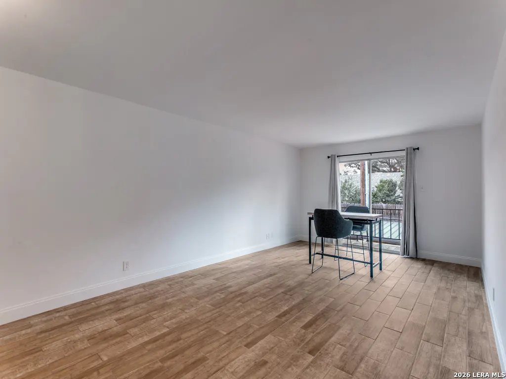 Bright, empty room with wood-look tile floor, white walls, and a table with two chairs near a sliding glass door.