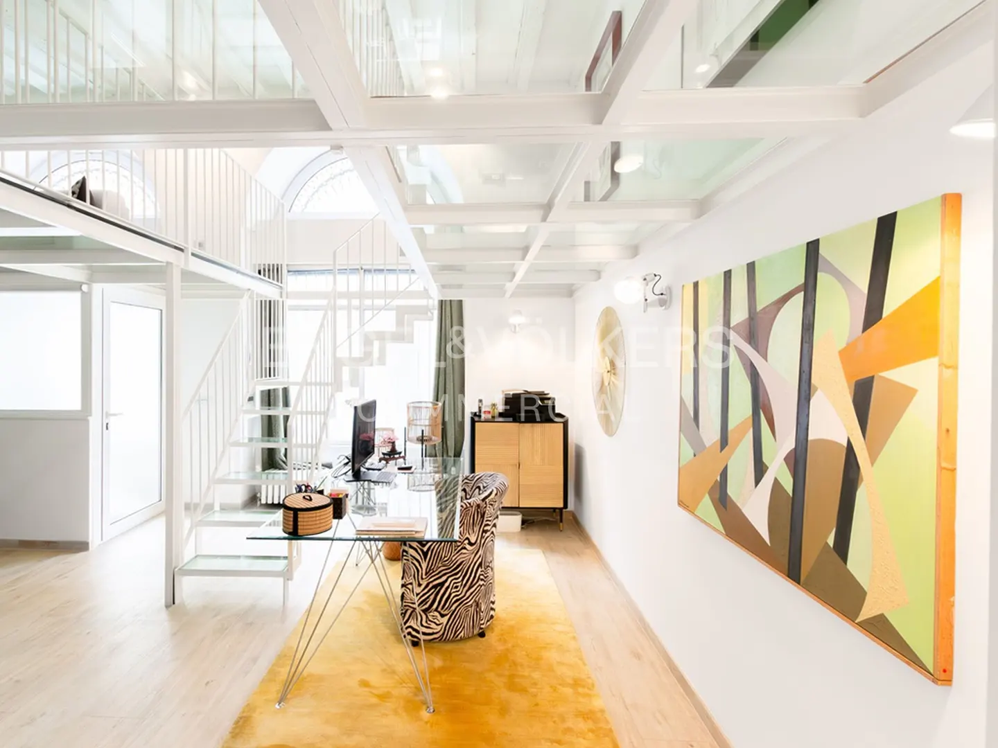 Bright, modern office space with white stairs, glass ceiling, desk, and zebra-print chair on a yellow rug. A large abstract painting hangs on the wall.