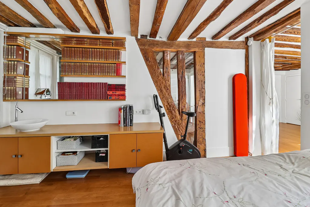 Bedroom with exposed wood beams, a sink on a cabinet with books above, and an exercise bike.