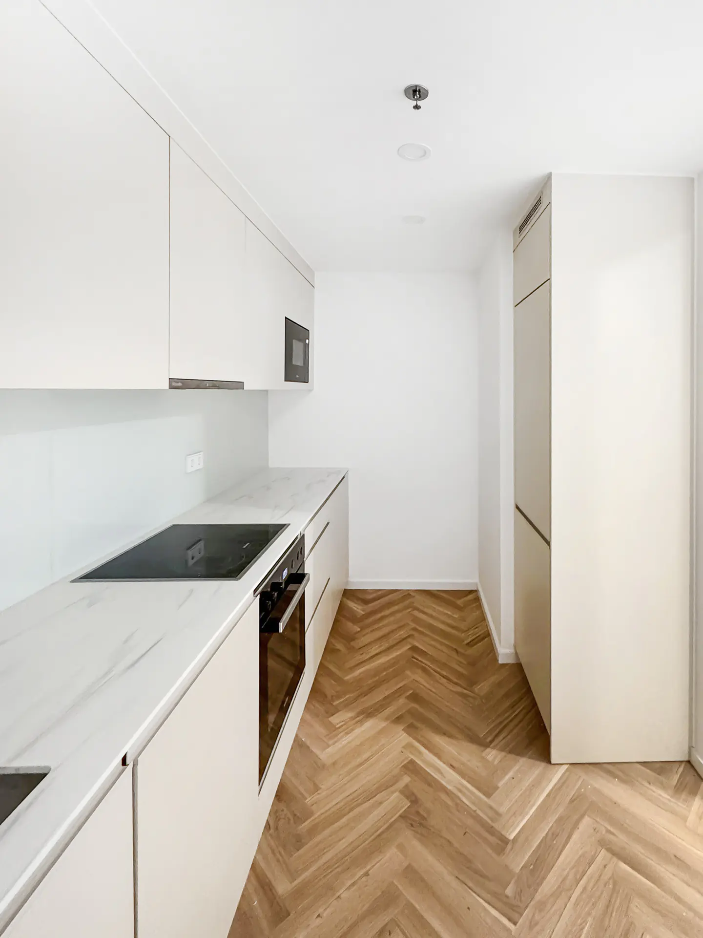 Bright kitchen with white cabinets, marble countertops, and herringbone wood floors. Oven, cooktop, and microwave are visible.