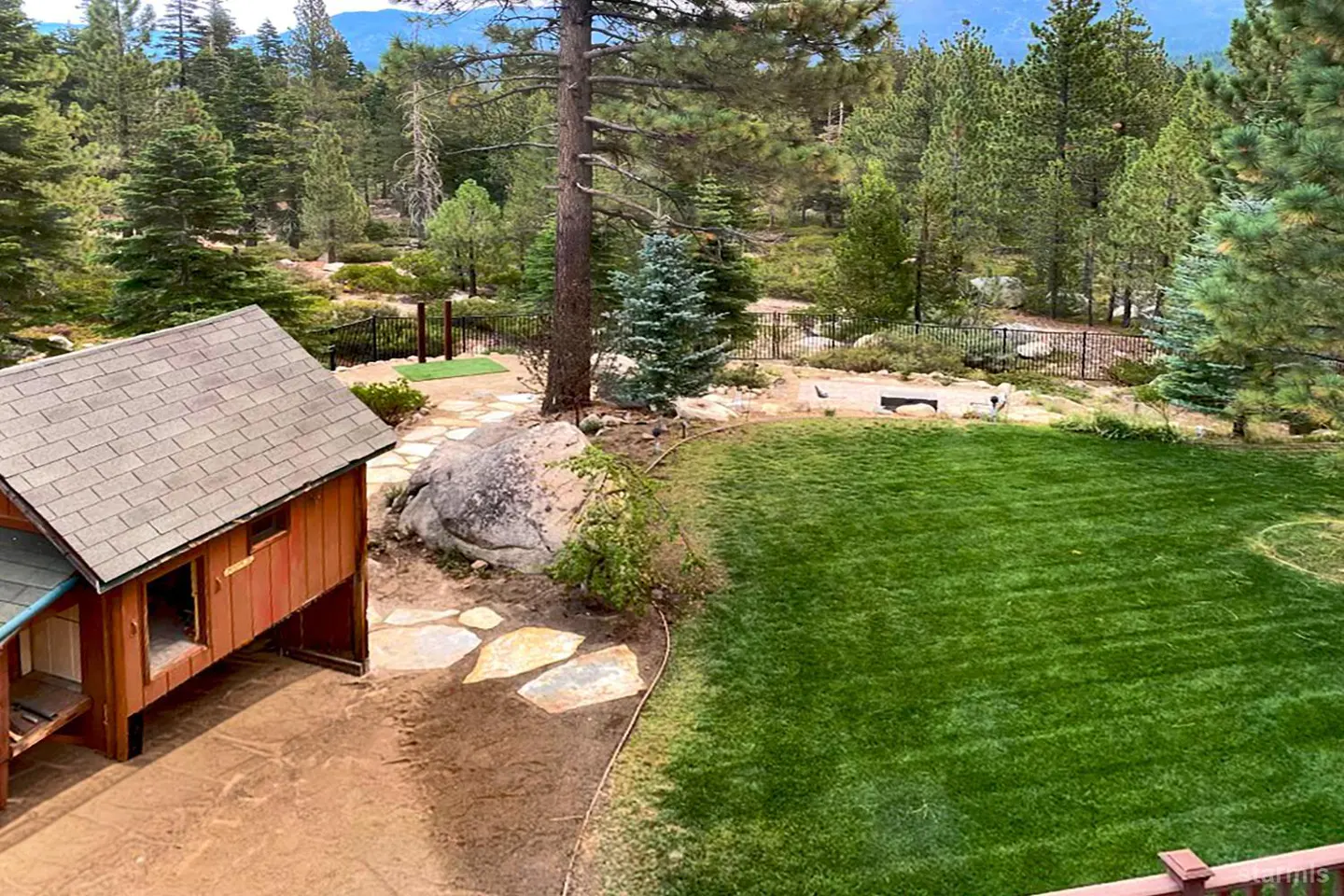 A backyard with a small wooden shed, a stone path, and a green lawn surrounded by trees.