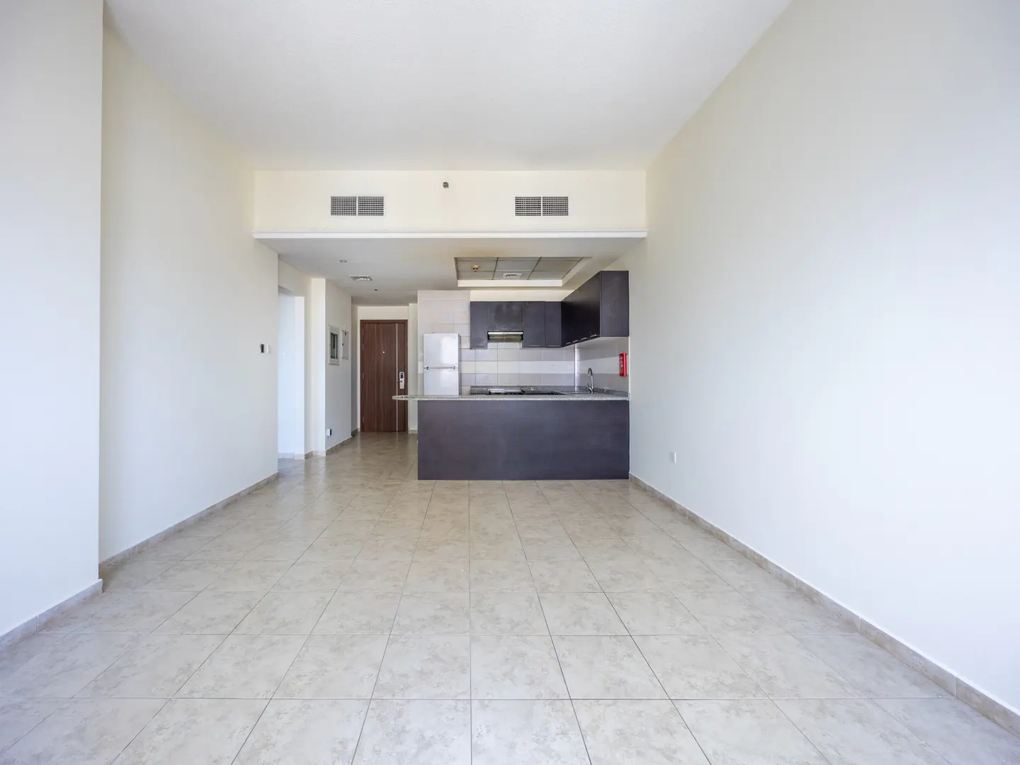 An open-concept apartment with beige tile flooring, white walls, and a dark gray kitchen island.