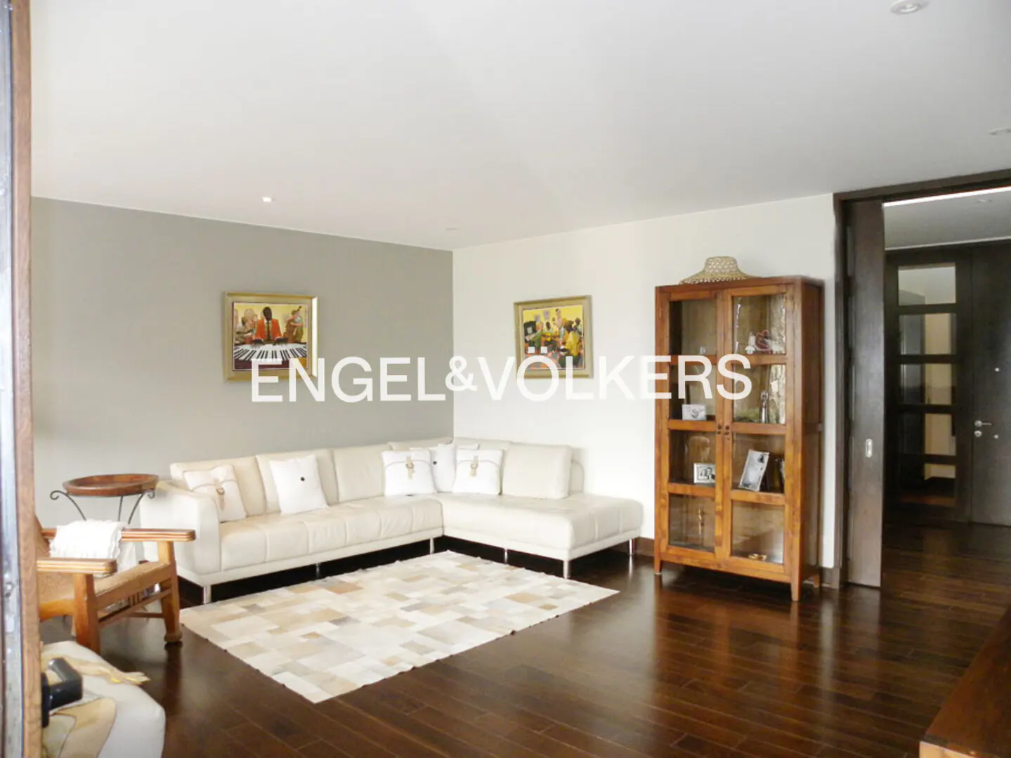 Living room with white sectional sofa, wooden display cabinet, patterned rug, and dark hardwood floors.