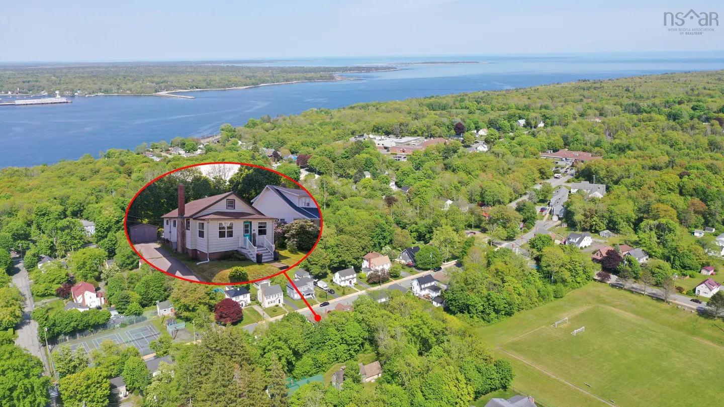 Aerial view of a white house circled in red, situated in a lush, tree-filled neighborhood near a large body of water.