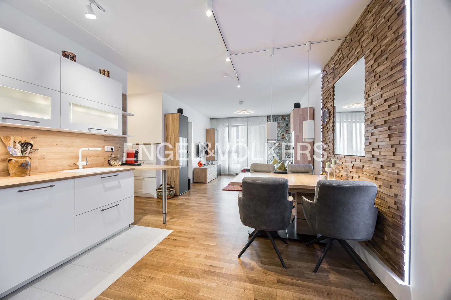 Bright, modern apartment with white cabinets, wood floors, and a dining area with gray chairs and a wood accent wall.
