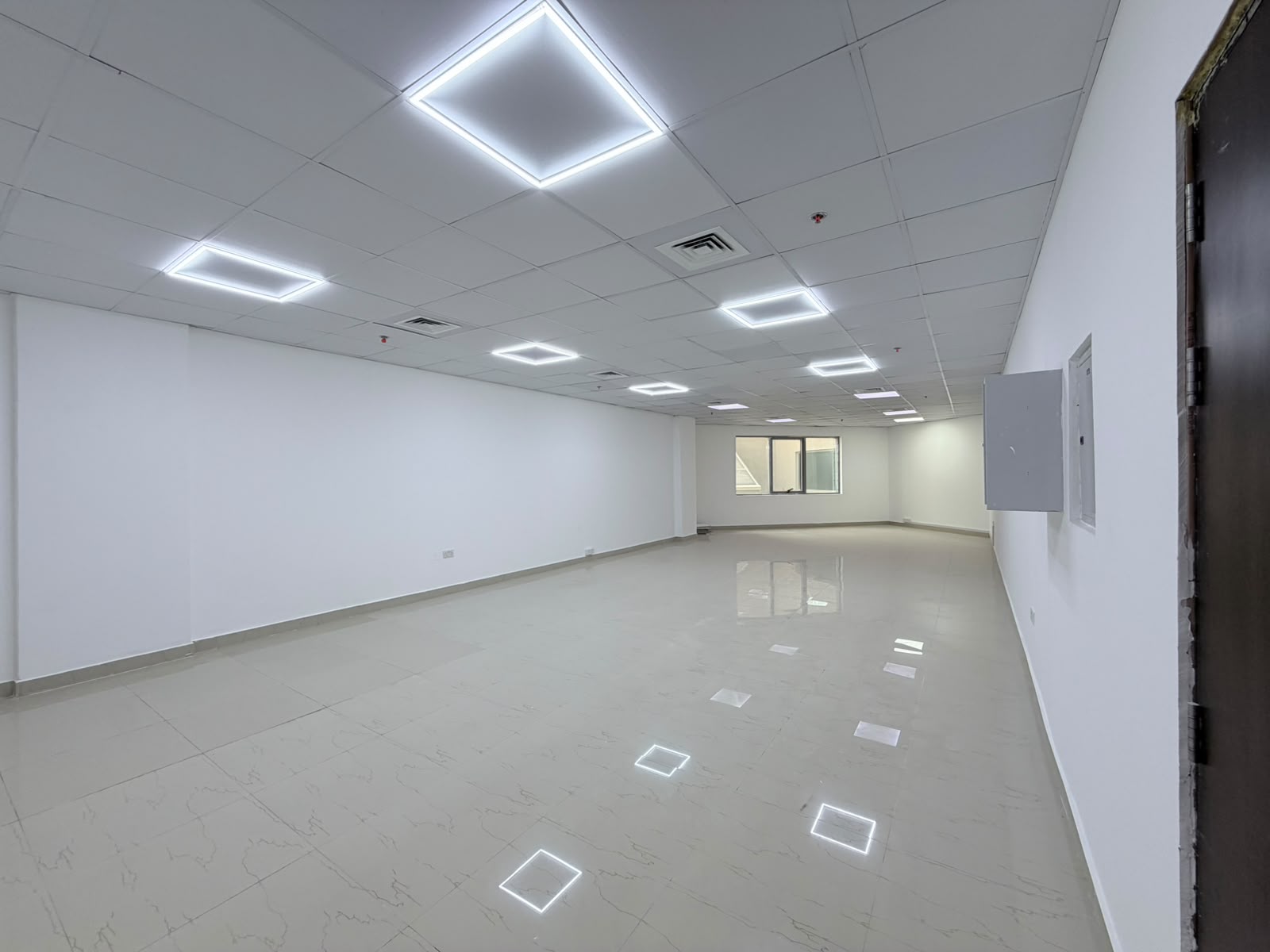 Empty, bright office space with white walls, glossy tiled floors, and square LED ceiling lights. [AI-generated text]