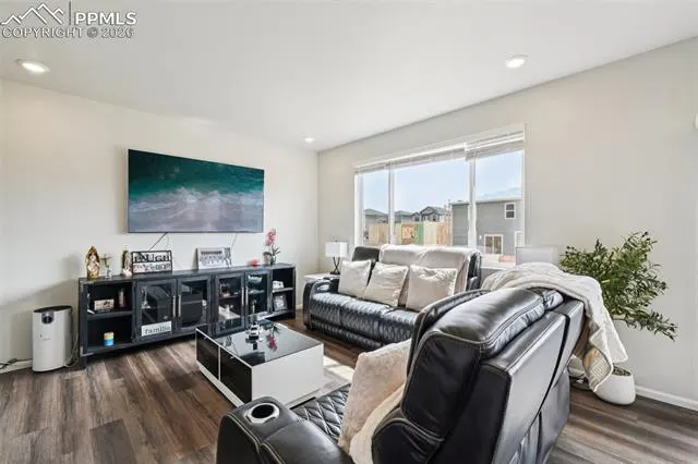 Living room with black leather sofas, a black and white coffee table, and a large TV on the wall. A window provides natural light.