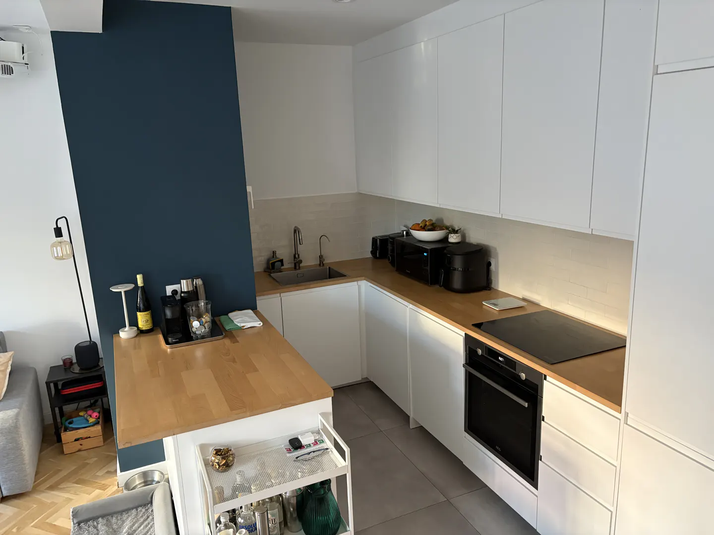 Bright kitchen with white cabinets, wood countertops, and a dark blue accent wall. A bar cart sits near a wooden table with drinks.