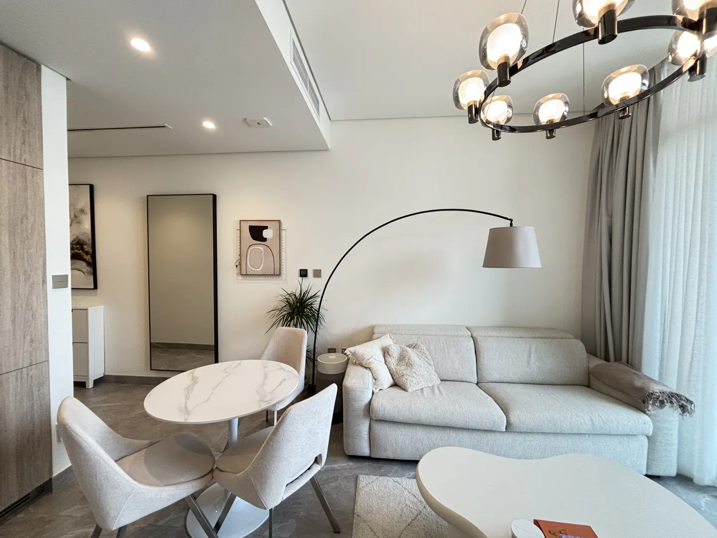 A modern living room with a round marble table, four chairs, a beige sofa, and a unique circular chandelier.